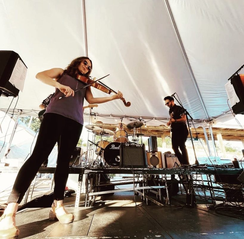 Brianna in sunglasses playing viola with a band under a white festival tent
